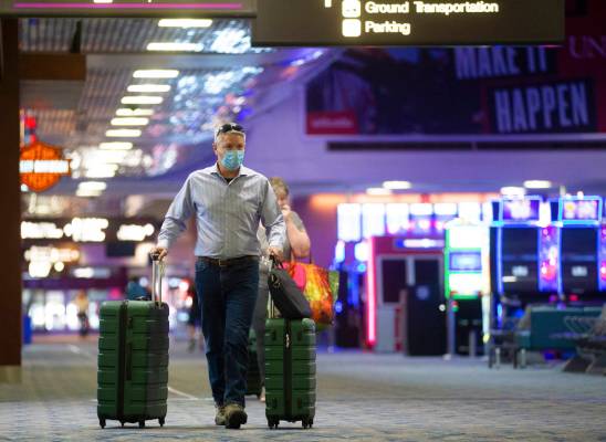 Travelers wearing protective masks make their way to their gate at terminal one at McCarran Int ...