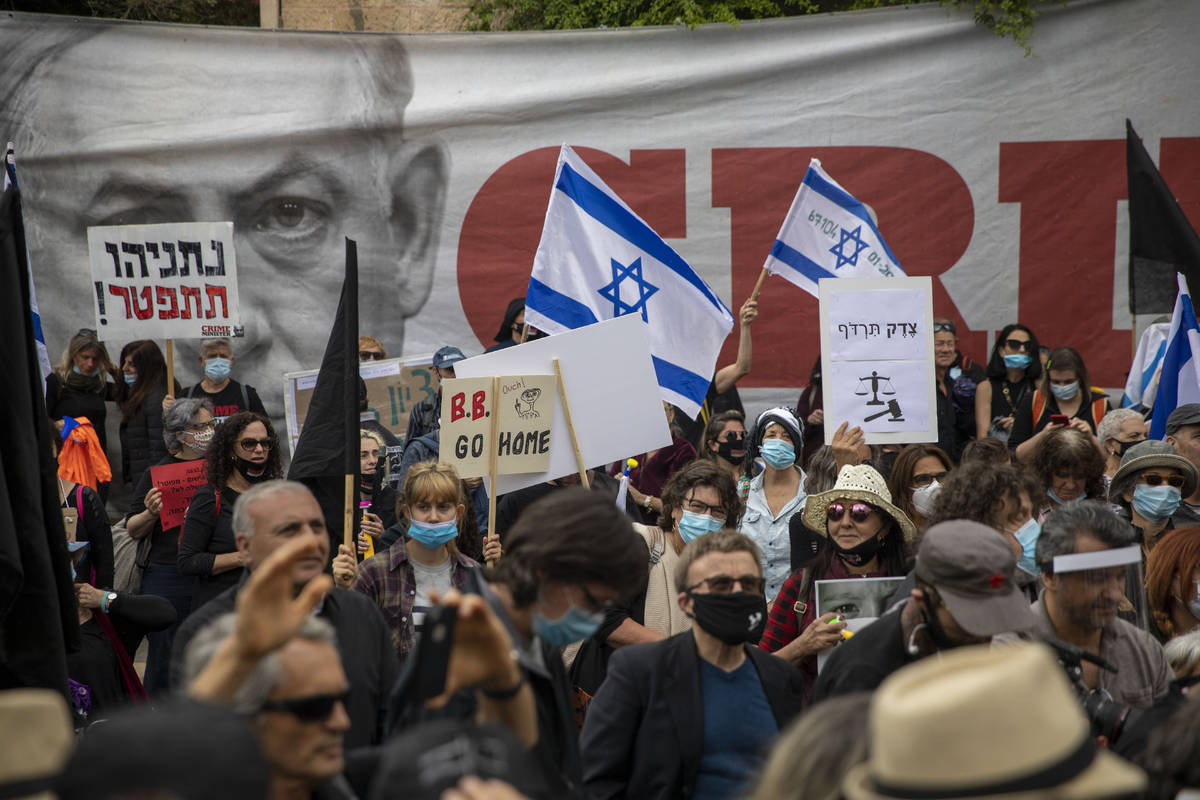 Protesters against Israel's Prime Minister Benjamin Netanyahu wave flags and banners outside hi ...