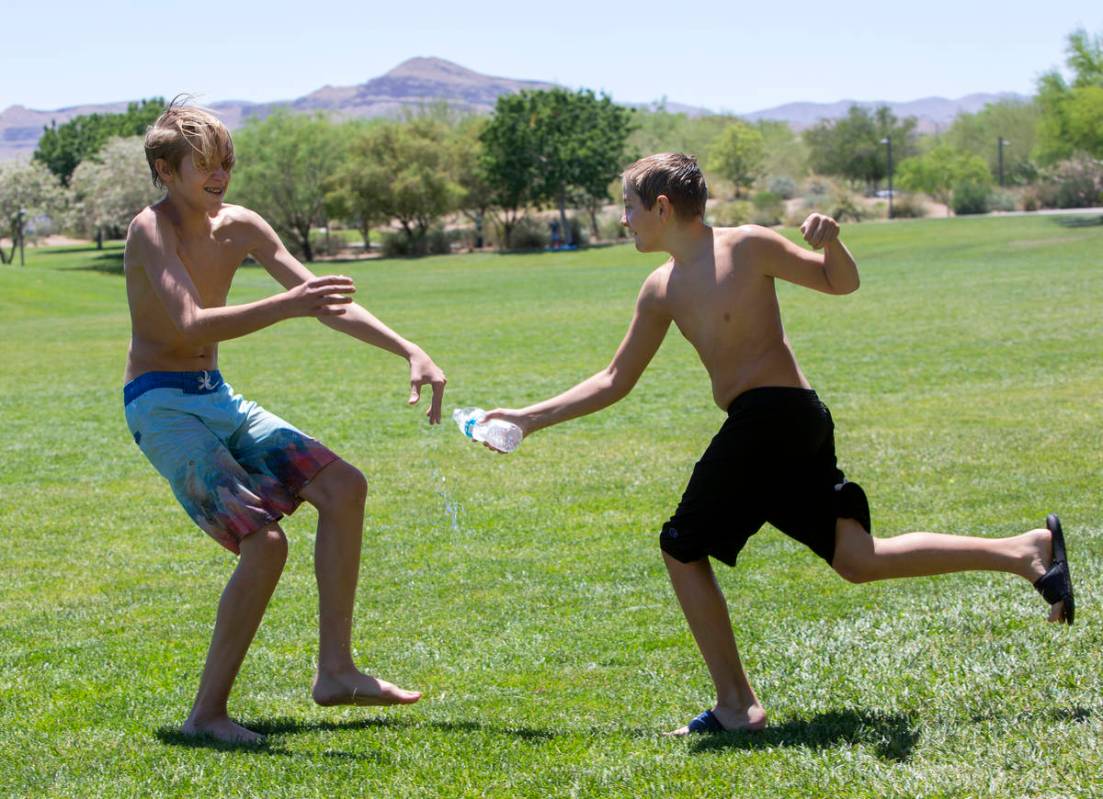 Chaz Henry, 14, runs away as Levi Henry, 12, splashes water on him at Exploration Peak Park on ...