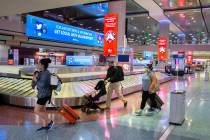 Travelers walk by new signage outlining coronavirus safety guidelines in the baggage claim area ...