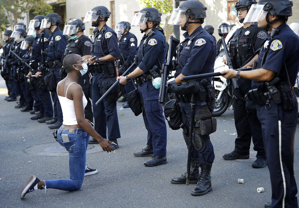 A masked protester kneels before San Jose police on Friday, May 29, 2020, in San Jose, Calif., ...