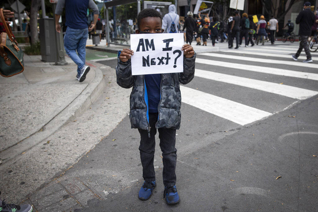 A boy holds a sign during a protest in downtown Los Angeles, Friday, May 29, 2020, over the dea ...