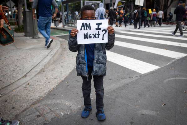 A boy holds a sign during a protest in downtown Los Angeles, Friday, May 29, 2020, over the dea ...