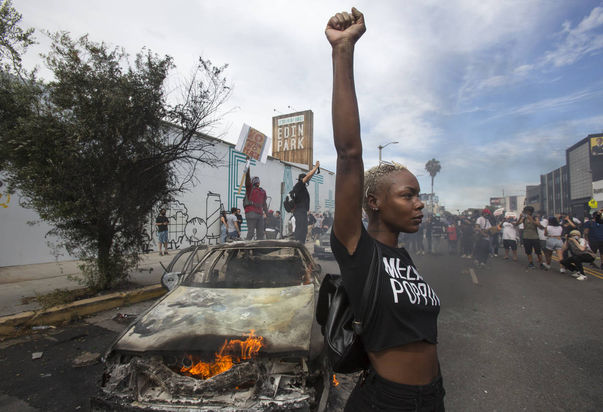 A protester poses for photos next to a burning police vehicle in Los Angeles, Saturday, May 30, ...