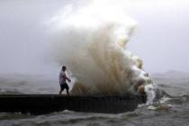 A wave crashes as a man stands on a jetty near Orleans Harbor in Lake Pontchartrain in New Orle ...