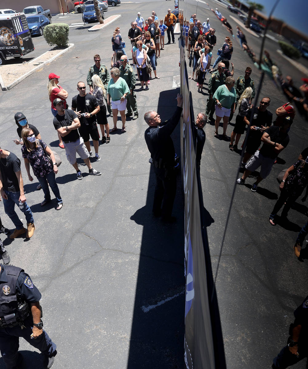 Henderson Police officer Sterling Candland signs the banner as people wait in line to buy T-shi ...