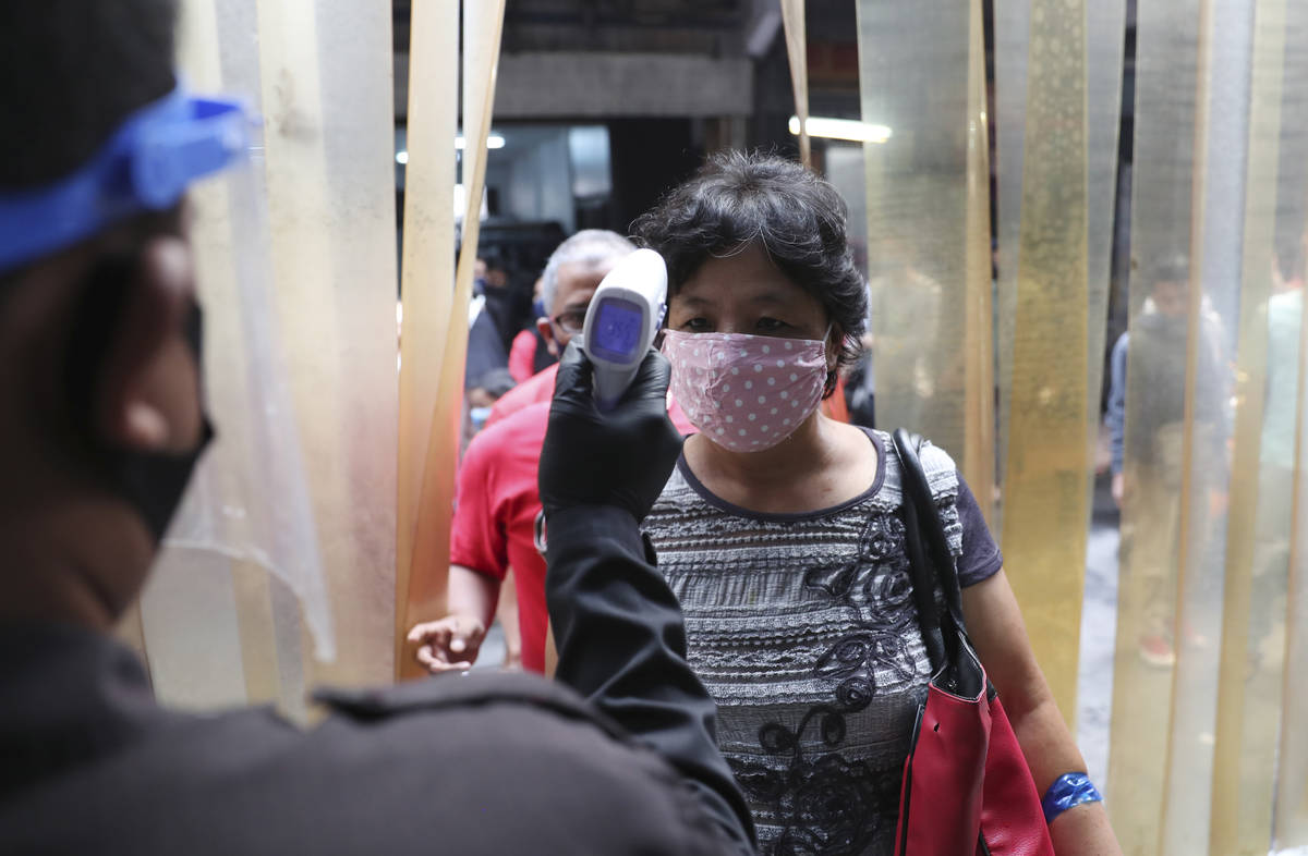 A security guard checks the body temperature of a woman before entering a clothing market to he ...