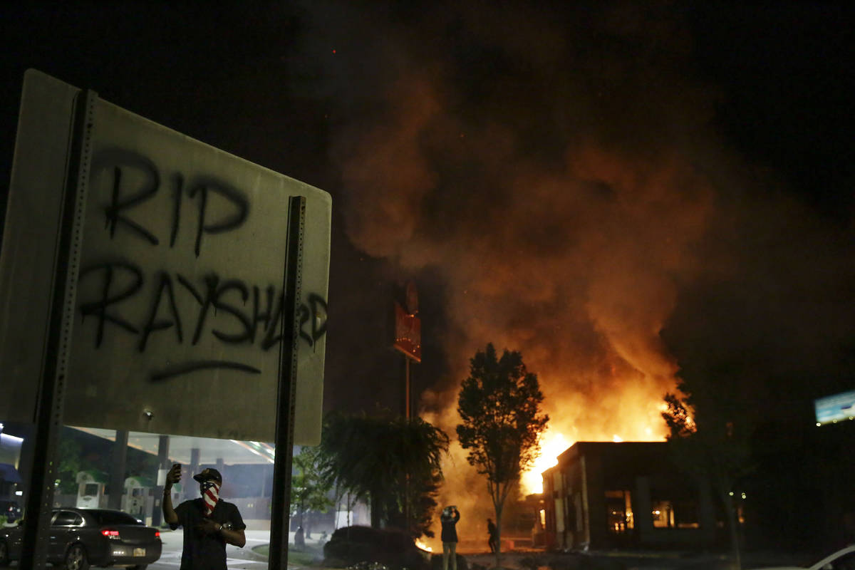 "RIP Rayshard" is spray painted on a sign as as flames engulf a Wendy's restaurant du ...