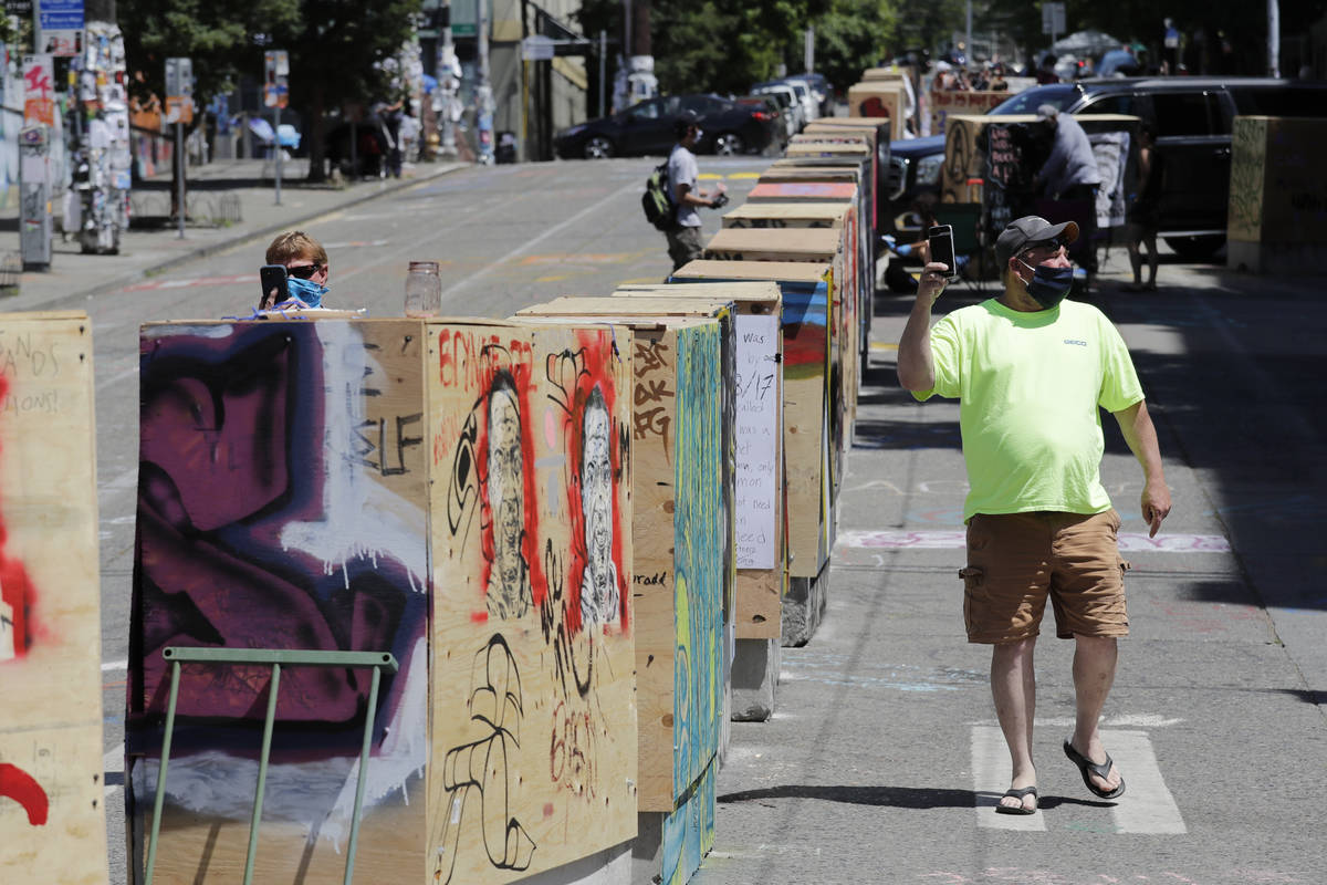 A man walks past barricades blocking a street adjacent to a closed Seattle police precinct Thur ...