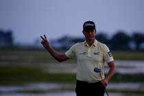 Webb Simpson waves as the sun disappears on the 18th green, on a course with no fans due to the ...