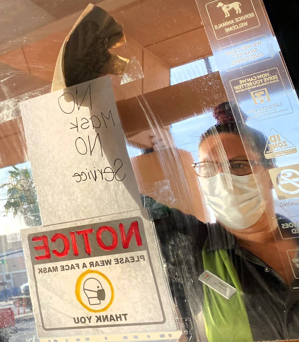 A clerk washes a window with a "No Mask No Service" sign at 7-11 on Las Vegas Bouleva ...
