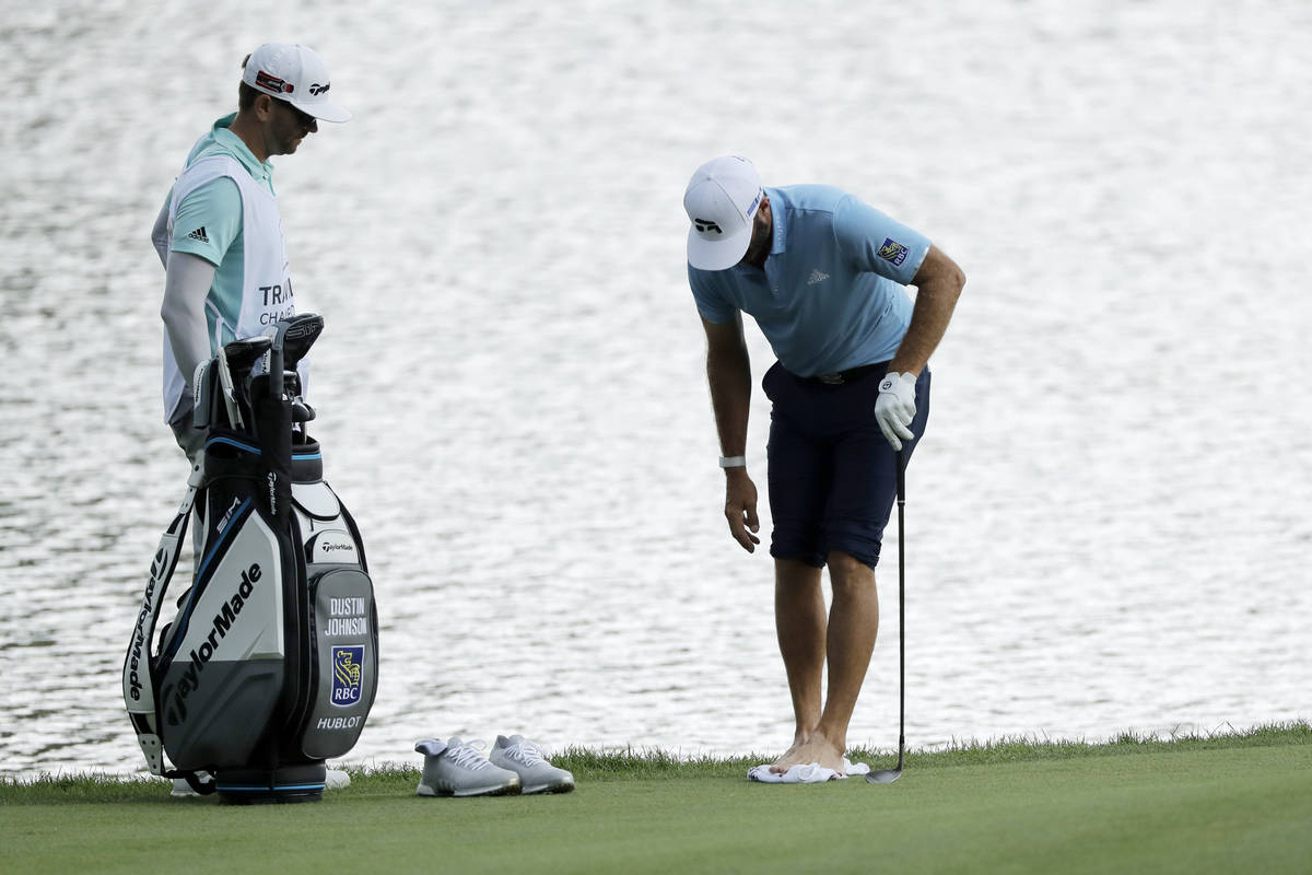 Dustin Johnson, right, cleans his feet after having to go in the pond to hit a ball on the roug ...