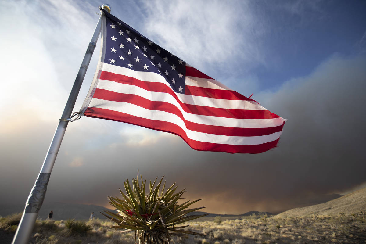 An American flag blows in the wind as the Mahogany Fire burns in the background at Mount Charle ...