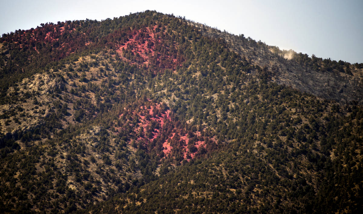 Fire retardant covers a hillside and fire smolders on the upside of it during the Mahogany Fire ...