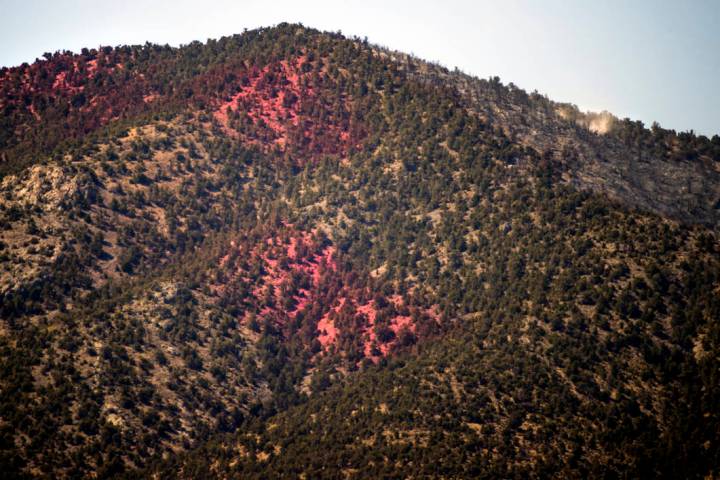 Fire retardant covers a hillside and fire smolders on the upside of it during the Mahogany Fire ...