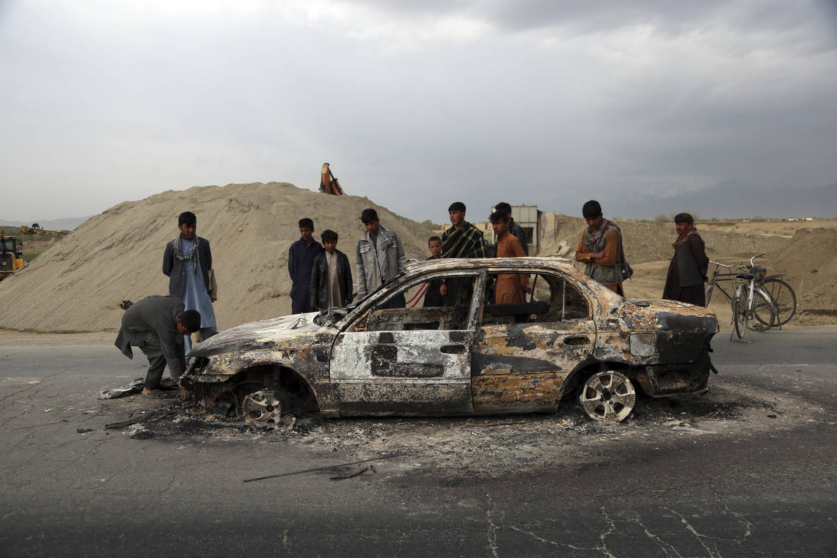 FILE - In this April 9, 2019, file photo, Afghans watch a civilian vehicle burnt after being sh ...