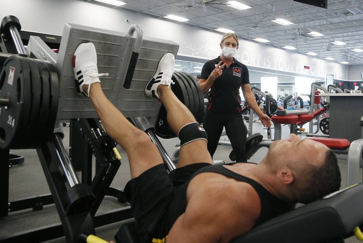 A trainer, top, at Mountainside Fitness, works with a client as the facility remains open even ...
