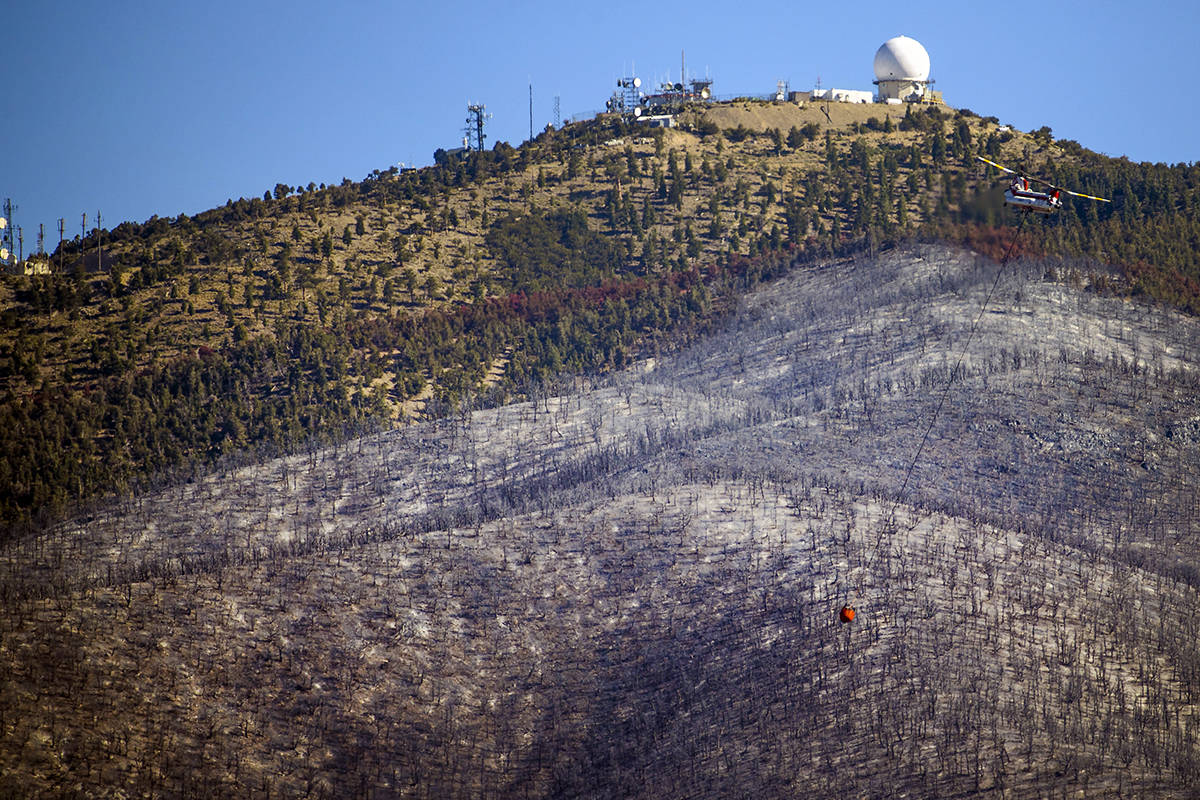 A helicopter with water bucket returns for another drop over the Mahogany Fire on Mount Charles ...