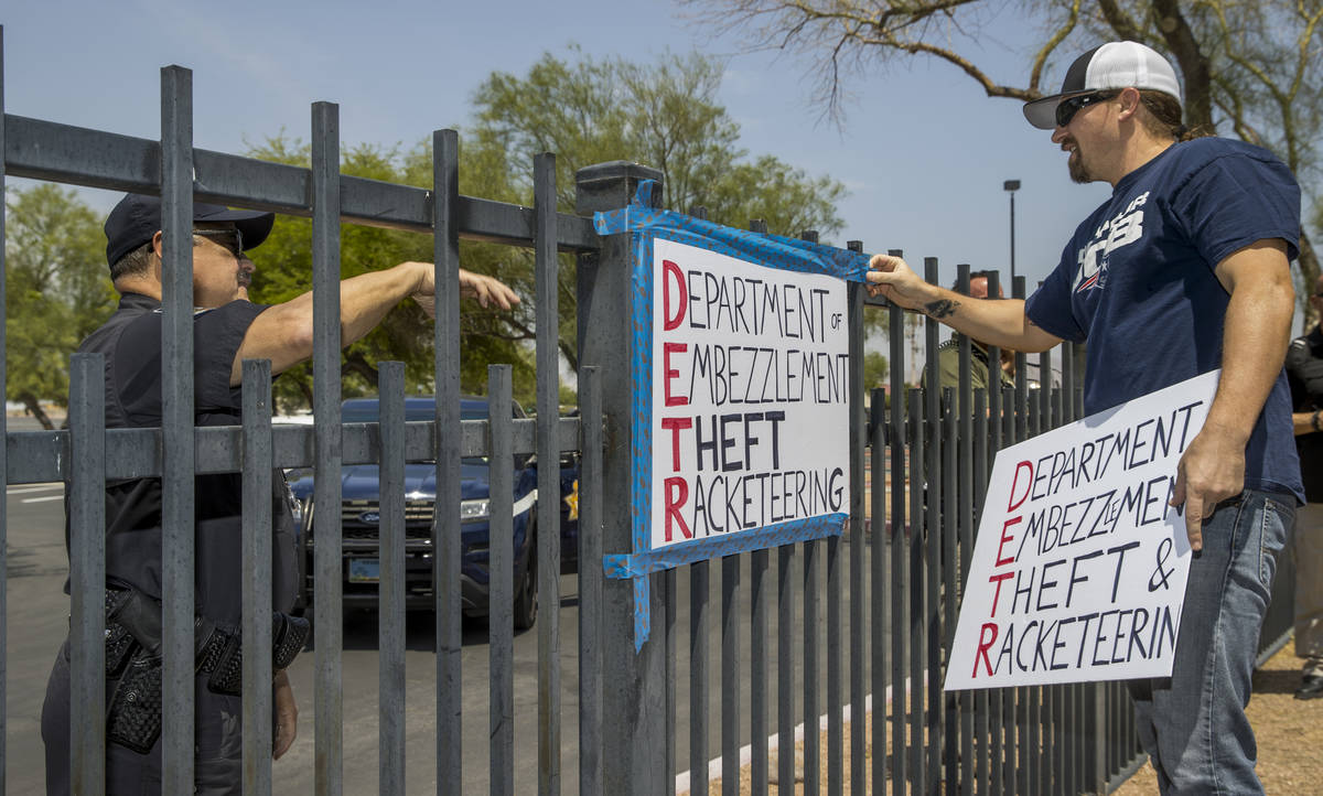 A security guard instructs Jon Berry, right, to take down a sign he attached to a fence in fron ...