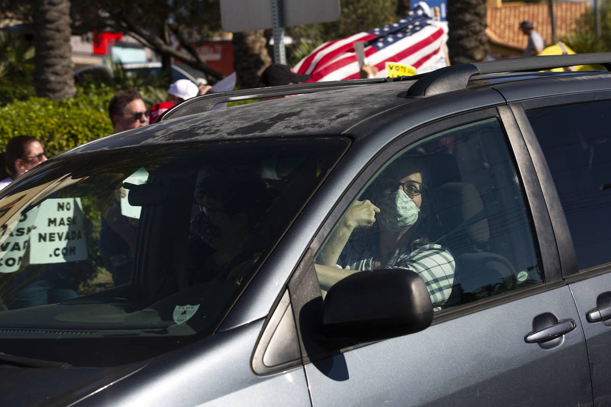 A passing motorist points to her mask as she passes the "No Mask Protest" at the inte ...
