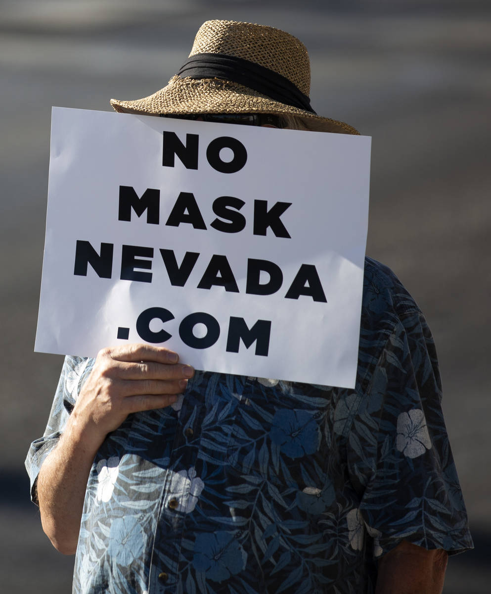 A protester covers his face with a sign during the "No Mask Protest" at the intersect ...