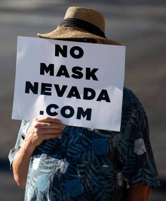 A protester covers his face with a sign during the "No Mask Protest" at the intersect ...
