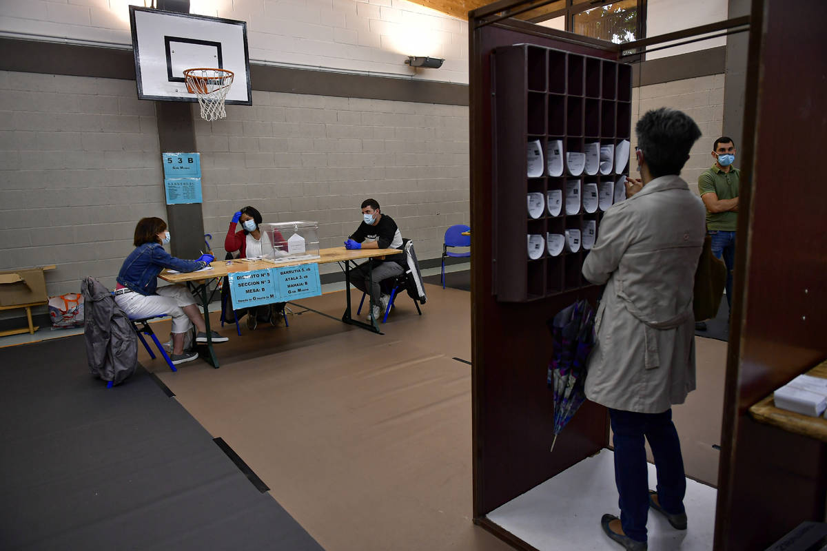 A woman prepares her vote while staff members of a polling station wear face masks to help curb ...