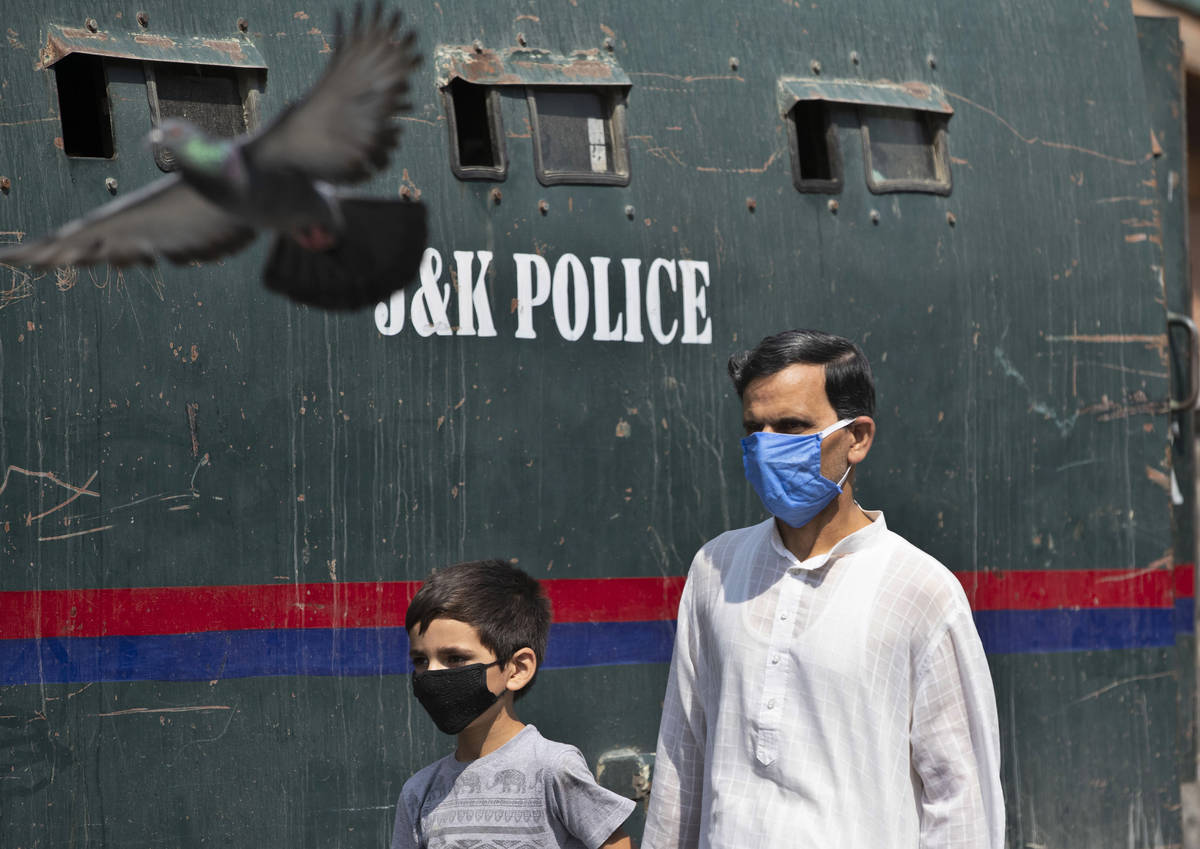 A Kashmiri man and a child wearing masks walk past a parked armored police vehicle in Srinagar, ...