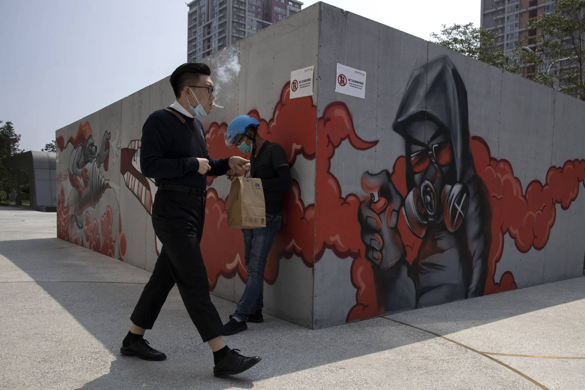 A man lowers his mask to smoke as he walks past graffiti artwork in Beijing Monday, July 13, 20 ...