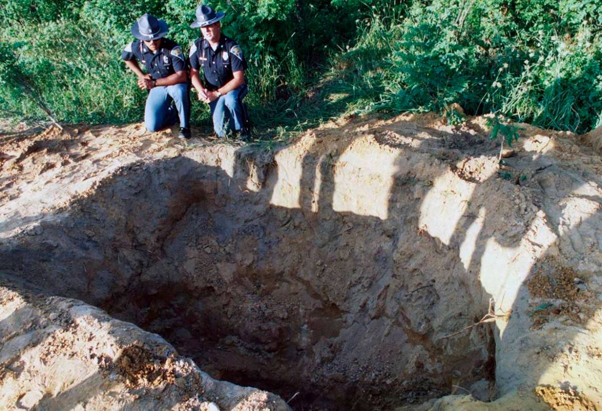 Two Indiana state troopers kneel at the edge of a grave where the bodies of reputed mobsters An ...