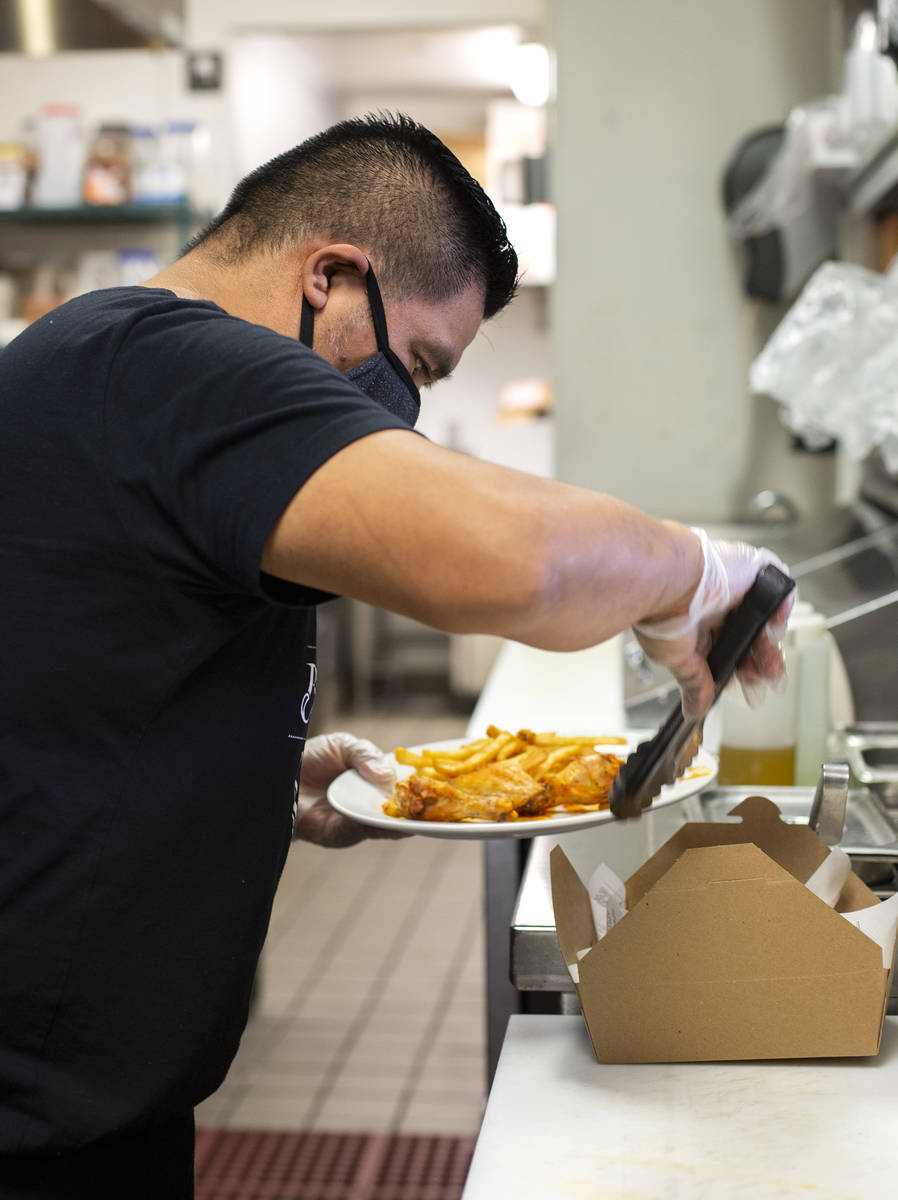Chef Armando Pescuul packages chicken wings and French fries into a to-go box at The Bling Pig ...