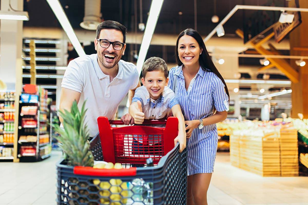 Happy family with child and shopping cart buying food at grocery store or supermarket