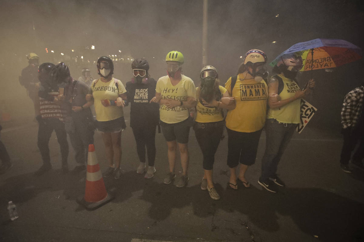 Members of the 'Wall of Moms' protest group lock arms as they are tear-gassed by federal office ...