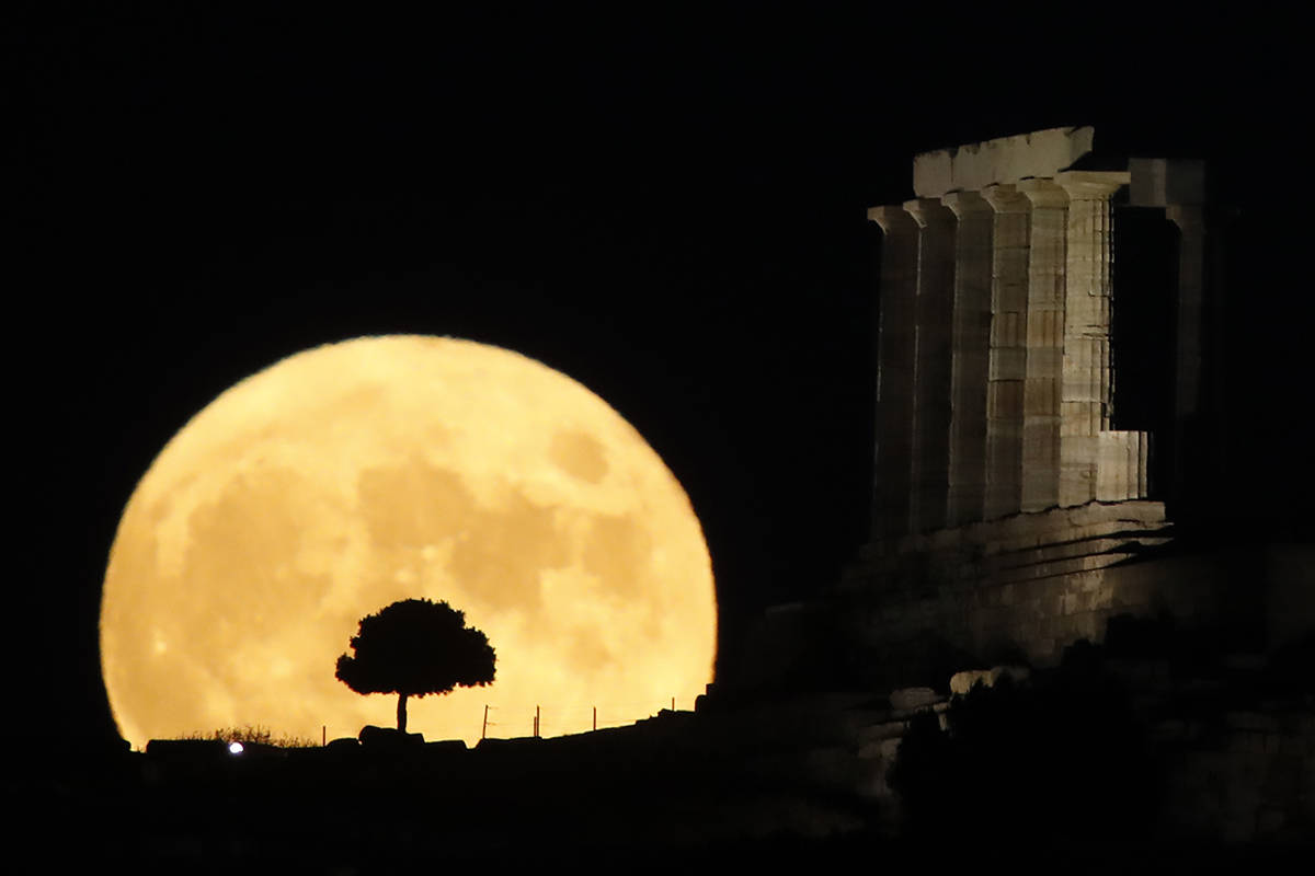 The moon rises behind the columns of the ancient marble Temple of Poseidon at Cape Sounion, abo ...