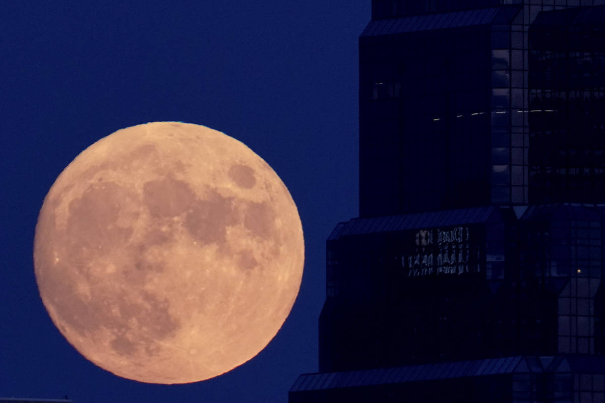 The full moon rises with an office building in the foreground, Sunday, Aug. 2, 2020, in downtow ...