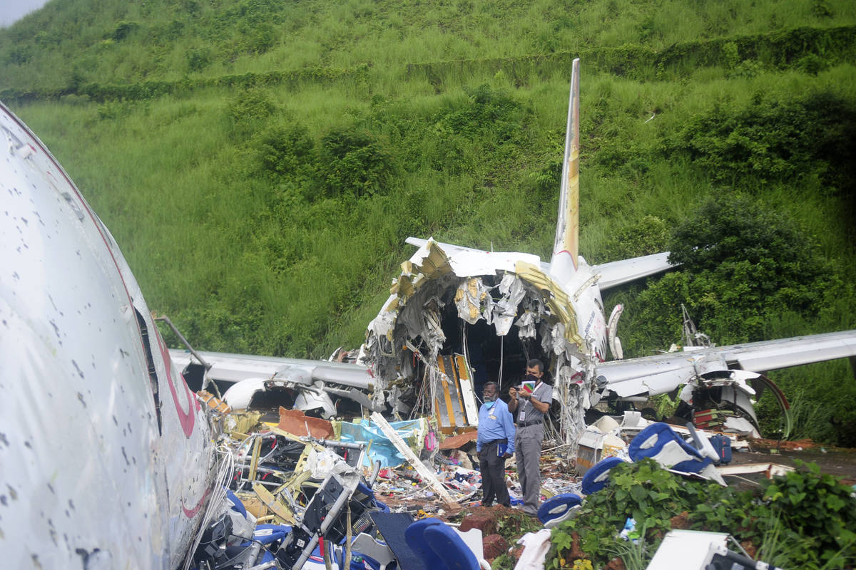 Officials stand on the debris of the Air India Express flight that skidded off a runway while l ...