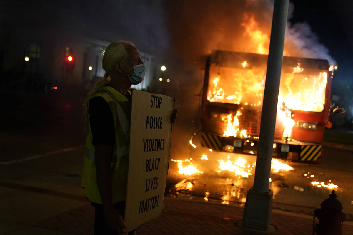 A protester stands near a burning garbage truck outside the Kenosha County Courthouse, late Mon ...