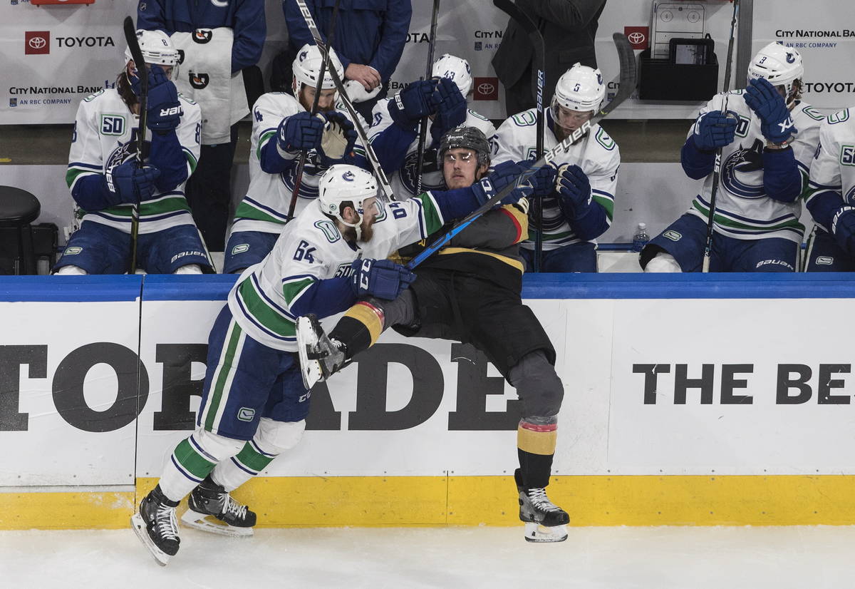 Vegas Golden Knights' Zach Whitecloud (2) is checked by Vancouver Canucks' Tyler Motte (64) dur ...