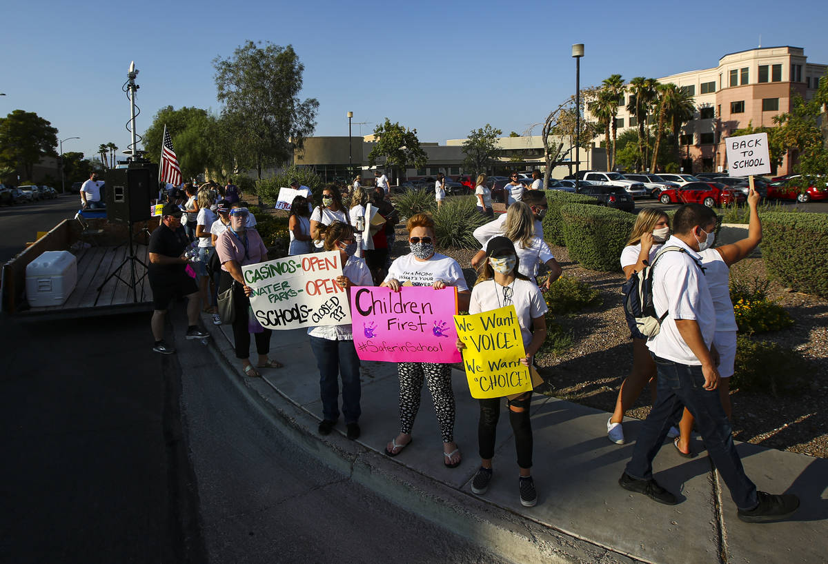 People hold up signs while participating in a demonstration in support of reopening public scho ...