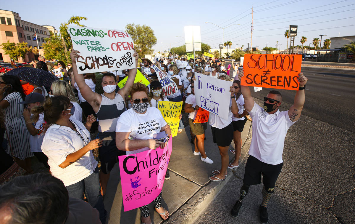 People hold up signs while participating in a demonstration in support of reopening public scho ...