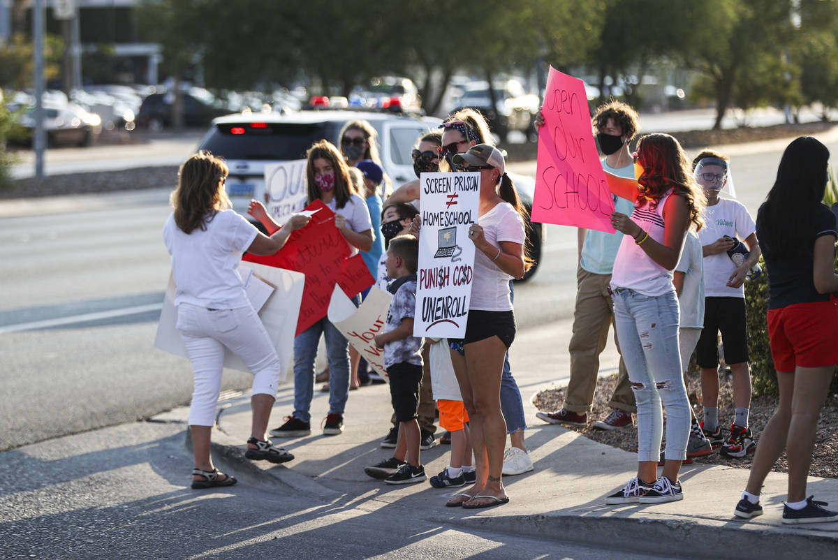 People hold up signs while participating in a demonstration in support of reopening public scho ...