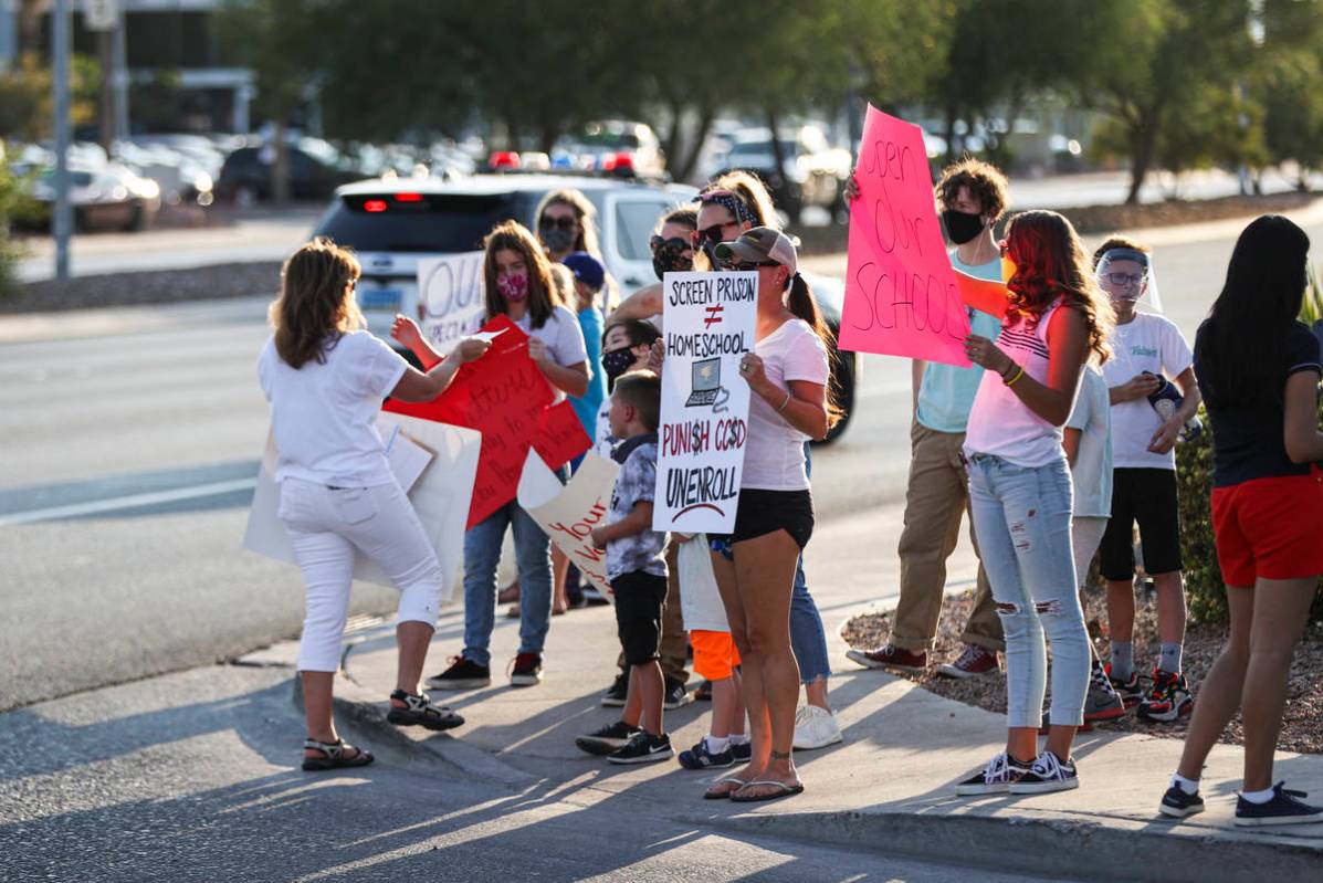 People hold up signs while participating in a demonstration in support of reopening public scho ...