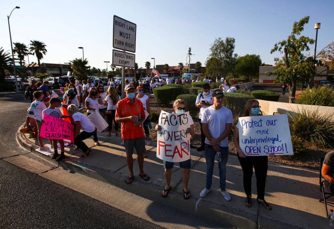 People hold up signs while participating in a demonstration in support of reopening public scho ...