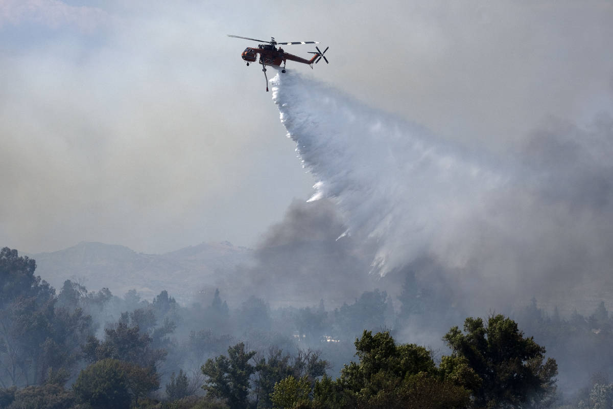 A Los Angeles fire department helicopter makes a water drop over a brush fire at the Sepulveda ...