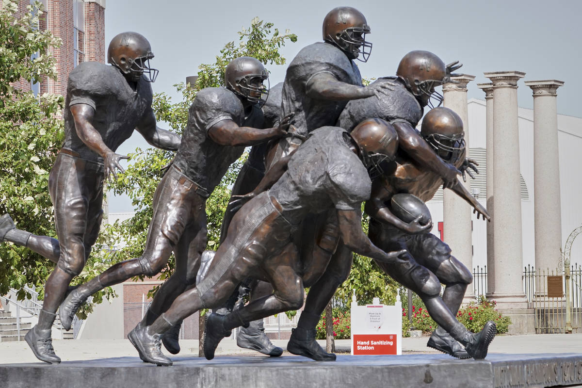 A hand sanitizing station is placed behind a statue of football players outside Memorial Stadiu ...