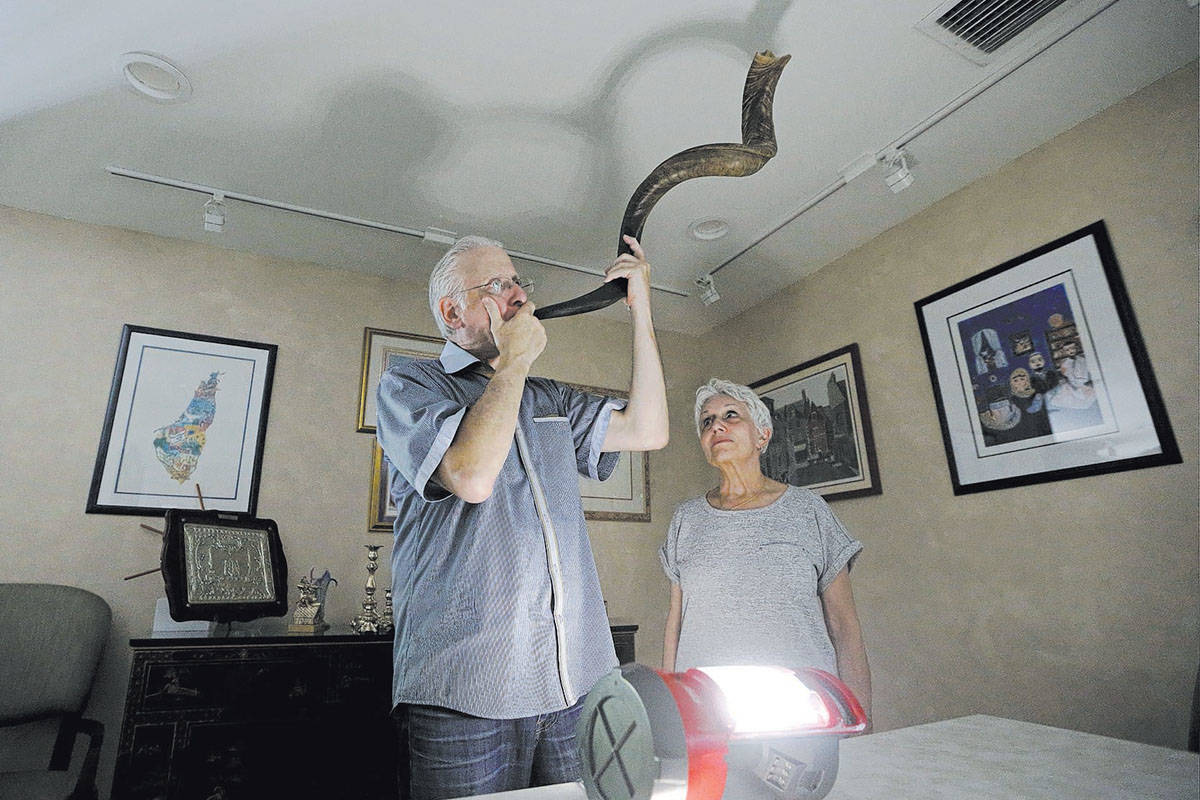 Michael Andron blows the shofar as he prepares for Rosh Hashanah, as his wife Lillian watches a ...