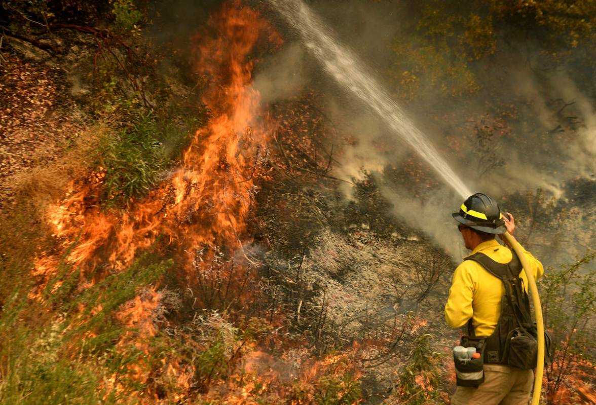 A firefighter puts out a hot spot along Highway 38 northwest of Forrest Falls, Calif., as the E ...