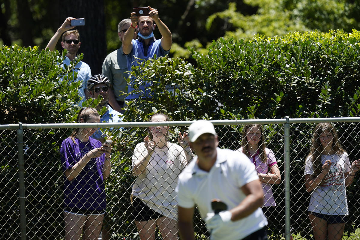 Fans watch from behind a fence as Brooks Koepka tees off on the second hole during the first ro ...