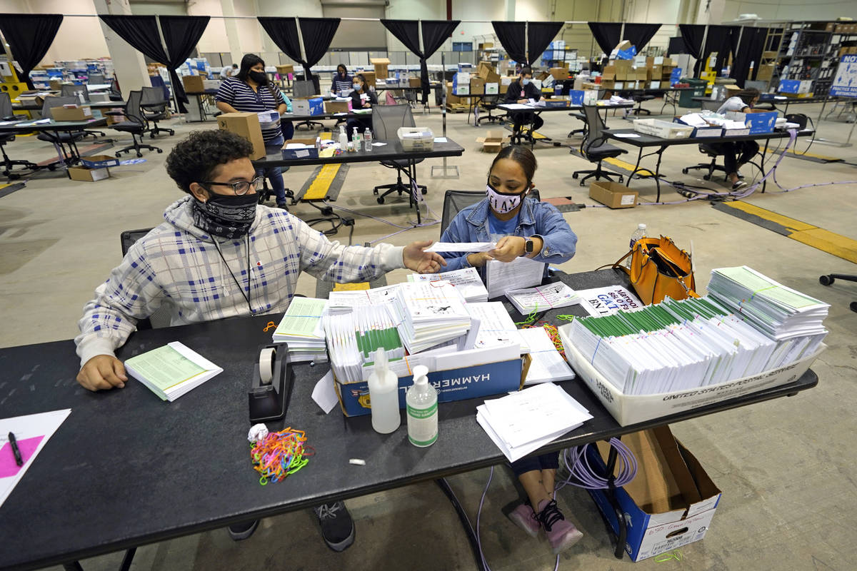 Harris County election workers Jose Vasquez, left, and Romanique Tillman prepare mail-in ballot ...