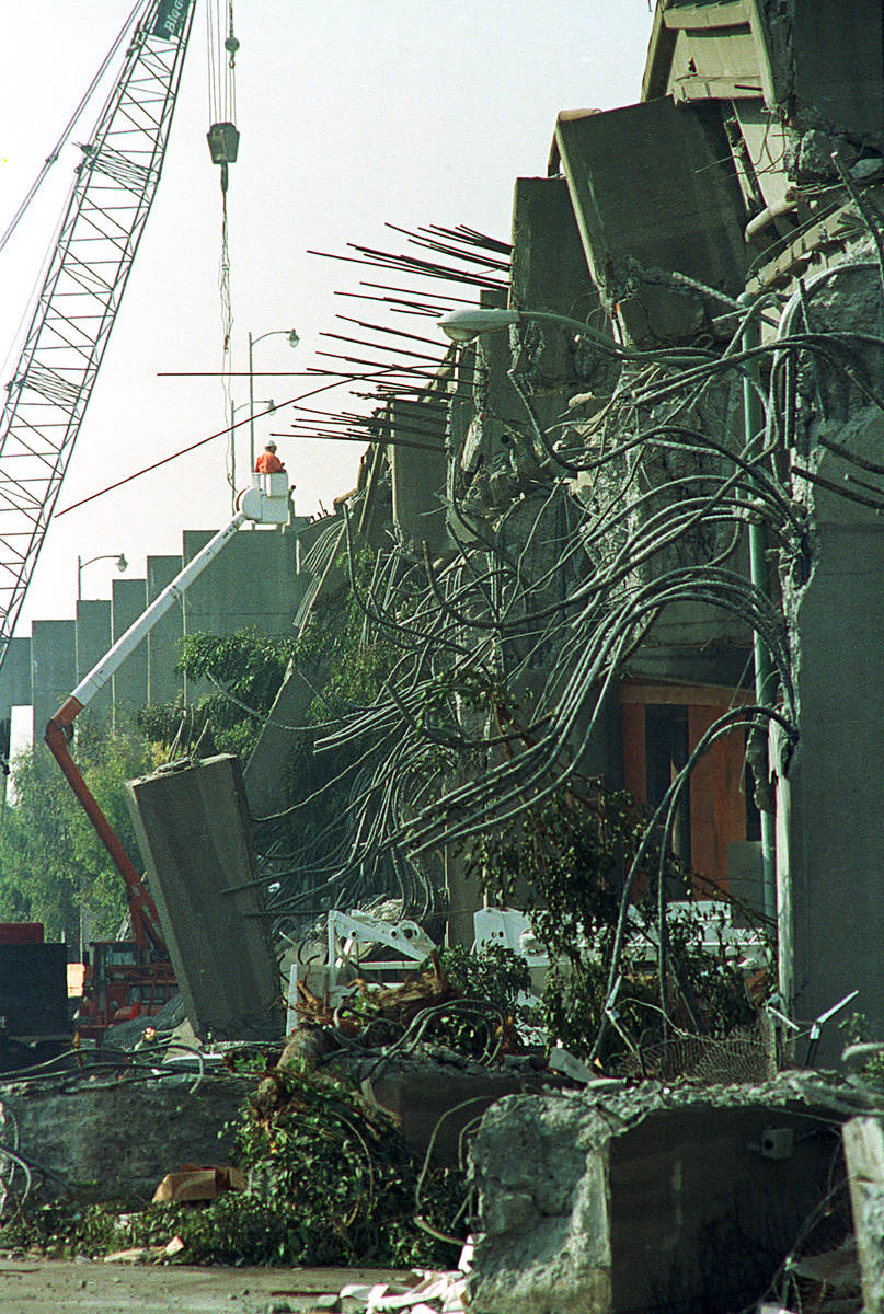 A crane lifts a worker as crews continue to clean up and search through twisted wreckage of the ...